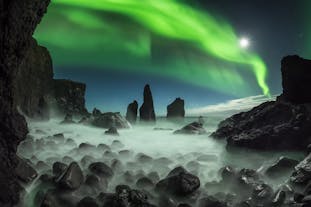 Northern Lights dancing over dark rock formations on the Reykjanes peninsula.