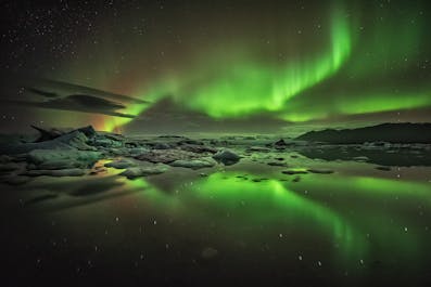 绿色的北极光在杰古沙龙冰河湖上空盘旋。
