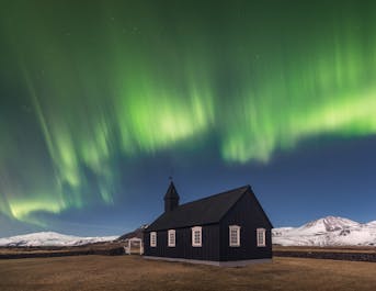 在冰岛的秋季，可以看到图片中的北极光在黑教堂Buðir后方翩翩起舞。