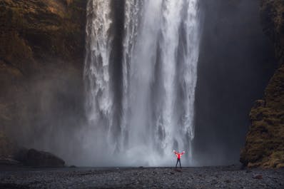Here, a visitor stands up close to the large waterfall Skógafoss; the ground leading up to the falls in exceptionally flat, allowing you to walk right up to the water.