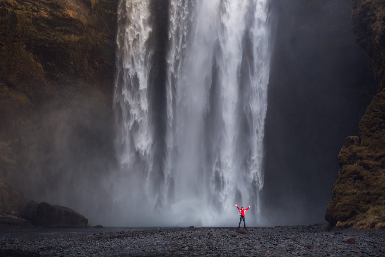 一位游客站在斯科加瀑布（Skógafoss）旁，通往瀑布的地面非常平坦，可以直接走到水边。