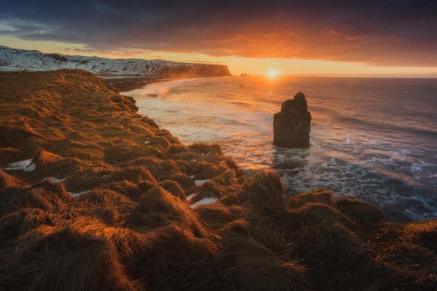 The sun setting over Iceland's South Coast dotted with dramatic sea stacks.