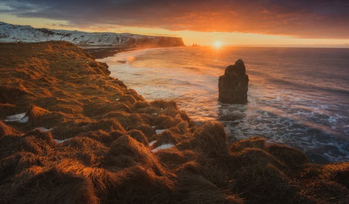 The sun setting over Iceland's South Coast dotted with dramatic sea stacks.