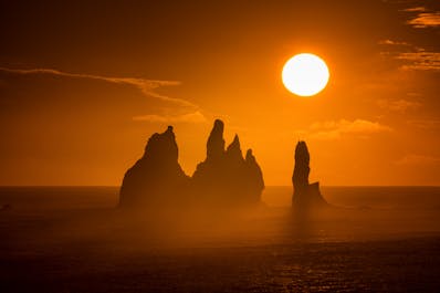 Il sole di mezzanotte splende sul mare, appena fuori dalla costa, sulla spiaggia di sabbia nera di Reynisfjara.