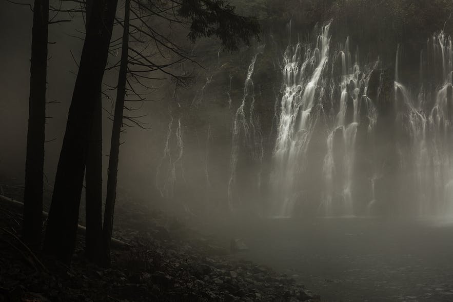 Silhouetted trees sit on the left while lines from a waterfall lie on the right - landscape Photography | Everything You Need To Know