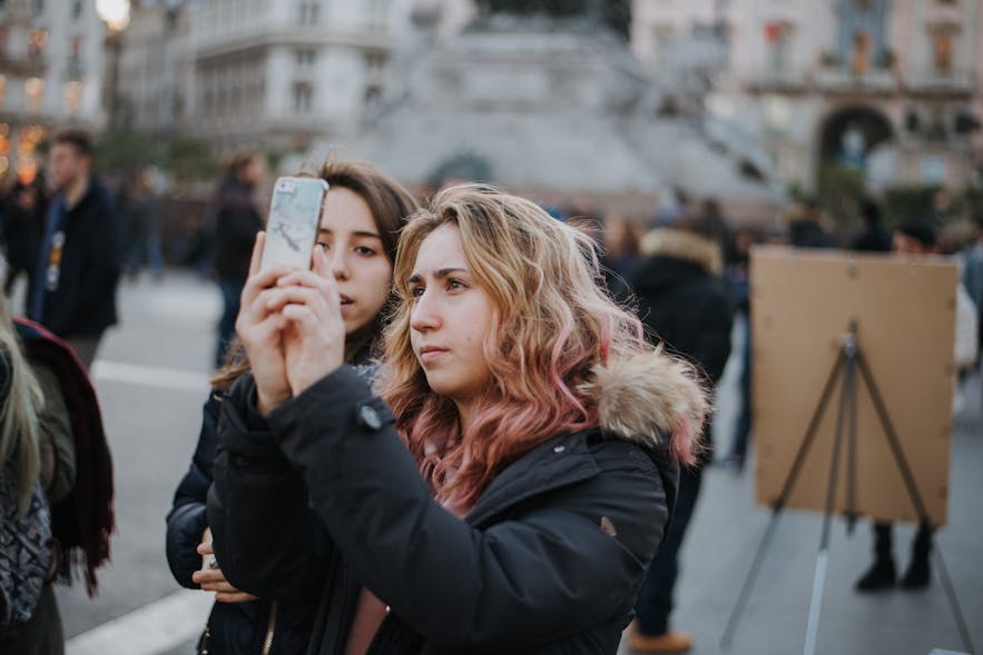 Two young women taking a photo in the streets with a smartphone.