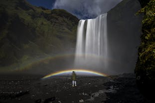 Majestic Skógafoss waterfall unveils its natural beauty, as the mist creates a vibrant rainbow, adding a touch of magic to the stunning landscape.