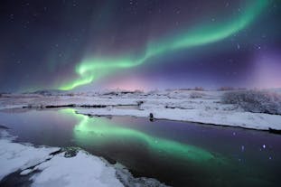 The northern lights produce a dazzling streak of color across the starry winter night sky, that reflects onto the water below.