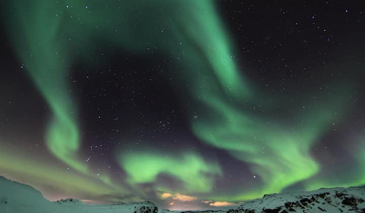 The aurora borealis produces dazzling formations of swirling green colors in the winter night sky, with a snow-covered landscape below.