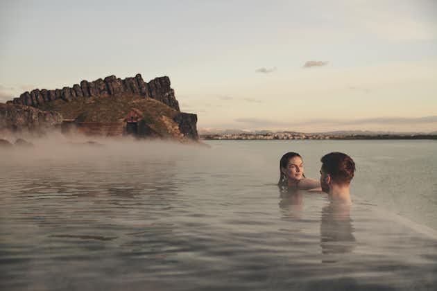 People relax at the Sky Lagoon pool's infinity edge, with a distant view of Reykjavik behind.