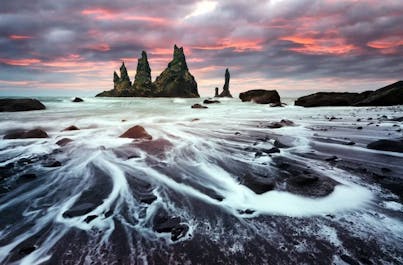 Reynisfjara's striking basalt columns rise like ancient sentinels against the roaring North Atlantic waves, a mesmerizing natural wonder.