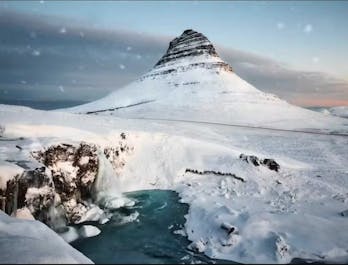 Kirkjufell stands tall, adorned in a shimmering cloak of snow, a breathtaking sight in Iceland's icy embrace.