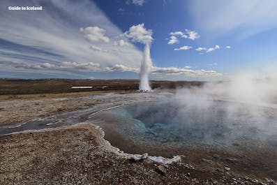 The Strokkur geyser erupts in the background at the Geysir geothermal area on a blue-sky summer's day.