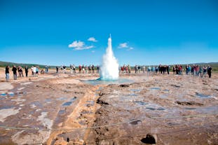 People stand near the Stokkur geyser as it erupts high into the air at the Geysir geothermal area on Iceland's Golden Circle sightseeing route.